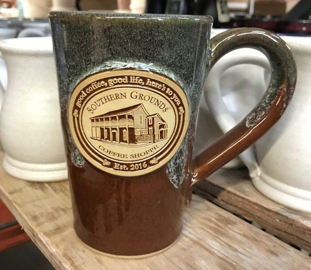 Brown and green tall coffee mug with an image of a building and the text "southern coffee grounds"