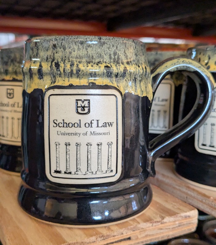 black mug with gold rim and a school of law logo on the mug